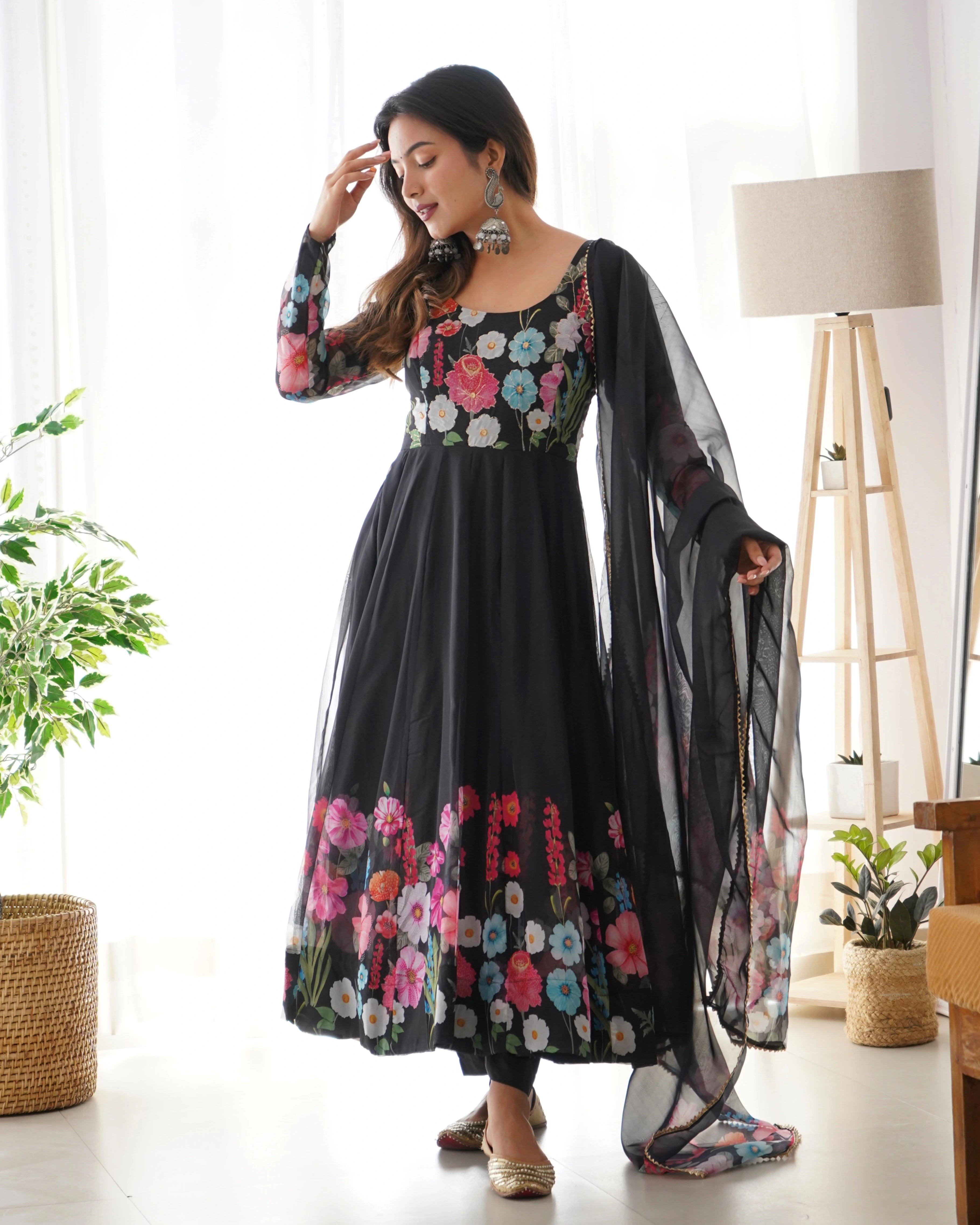 Woman wearing a black floral dress with a sheer dupatta in a bright room.
